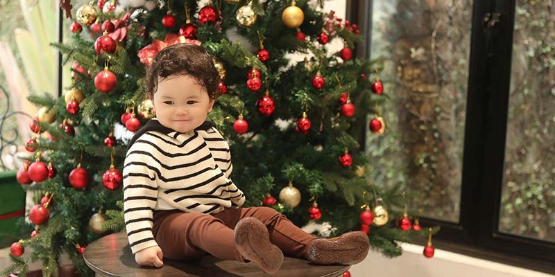 menininho sentado em frente a uma árvore de natal