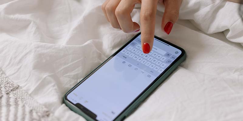 mão de pessoa usando o celular sobre uma superfície branca