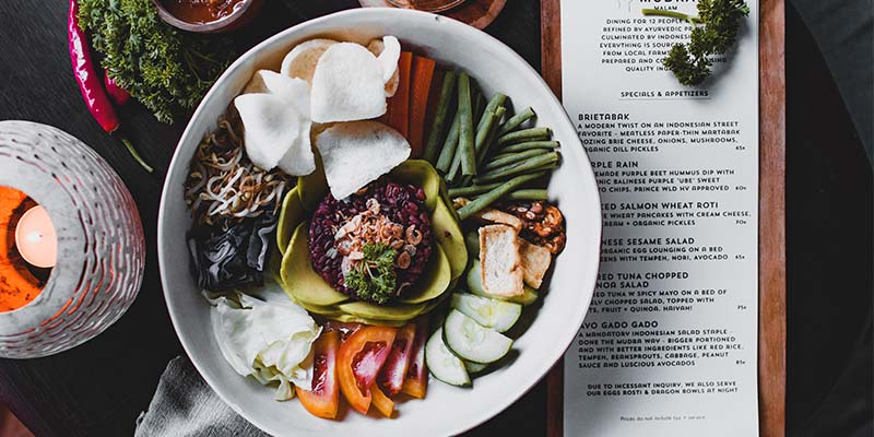 Mesa de um restaurante vista de cima com um prato de legumes e um cardápio ao lado