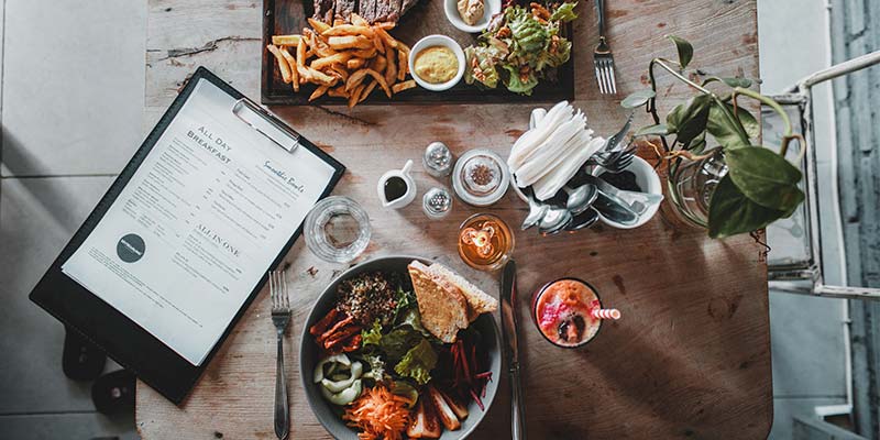 Mesa de um restaurante vista de cima com algumas porções de alimento e um cardápio