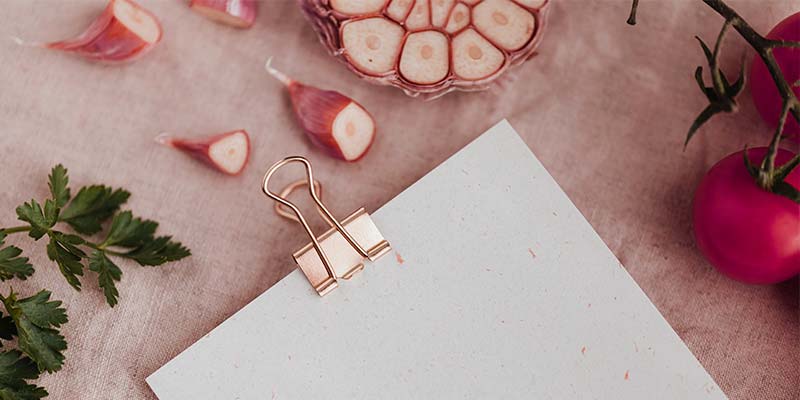 Dentes de alho e uma prancheta branca sobre uma mesa rosa