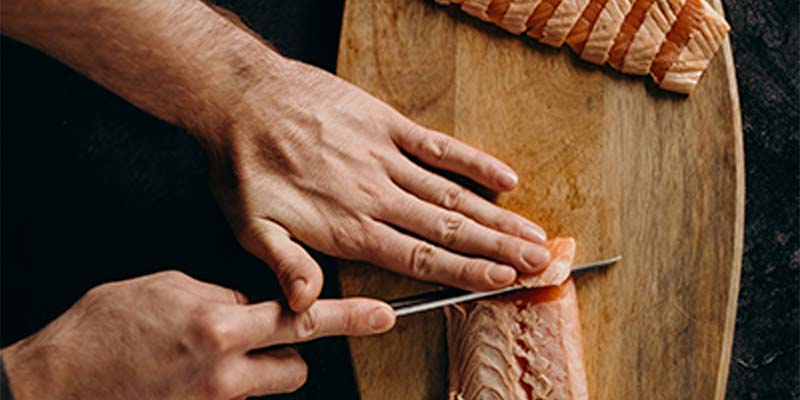 Mãos de uma pessoa cortando carne em uma tábua