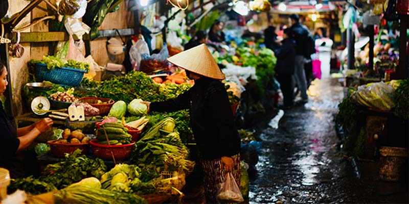 Mulher em feira de rua comprando verduras a noite