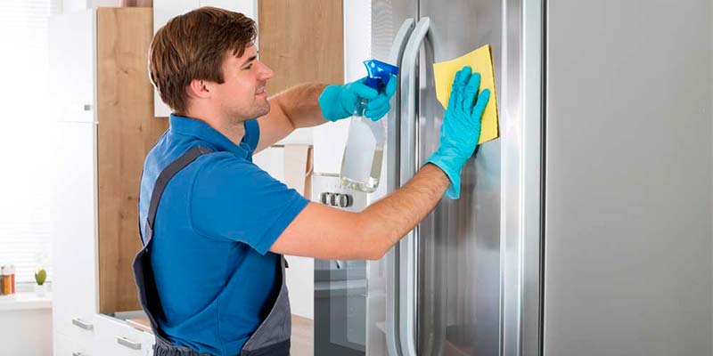 Homem de avental e luvas limpando a parte externa da geladeira com um pano