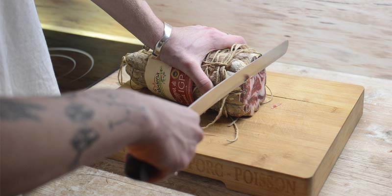Pessoa cortando carne com uma faca grande em uma tábua de madeira