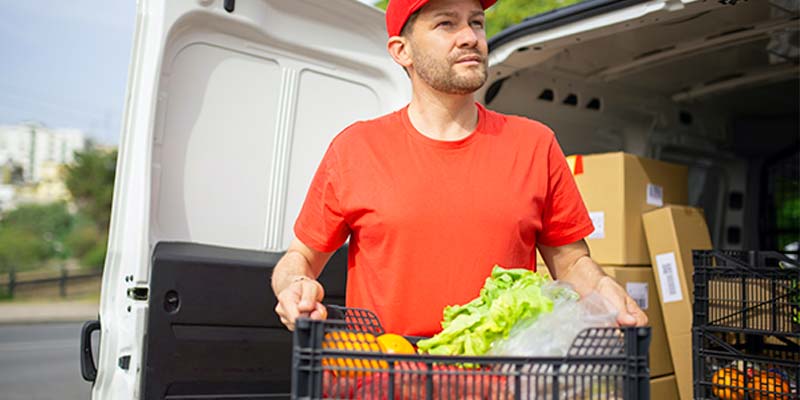 Homem de uniforme vermelho retirando uma caixa de produtos de uma van