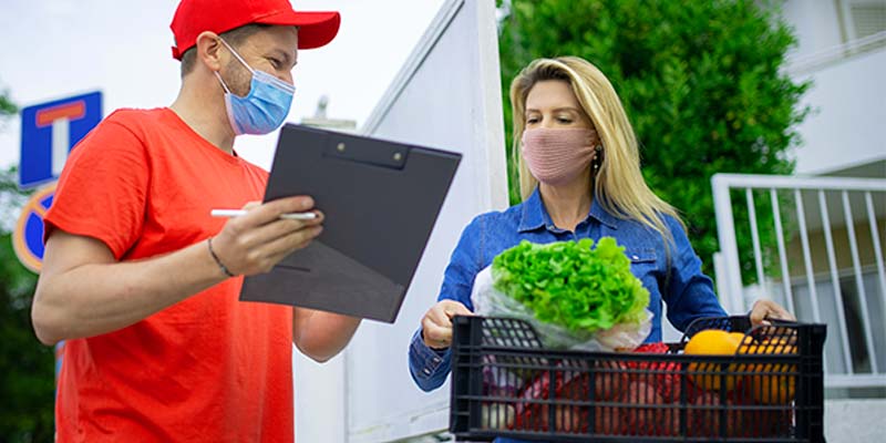Mulher recebendo a caixa de produtos ao lado do homem de uniforme vermelho