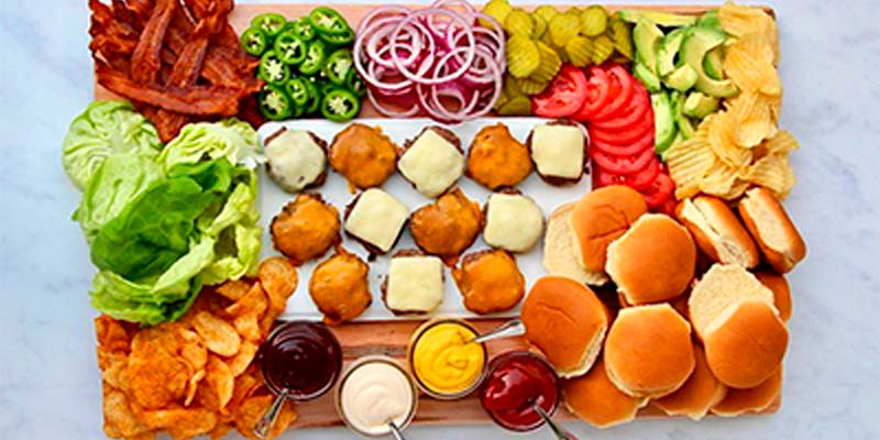 Tábua com ingredientes para ser feito um hamburguer e com diferentes tipos de molhos