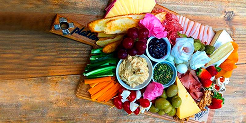 Tábua de frio com diferentes tipos de alimento sobre uma mesa marrom