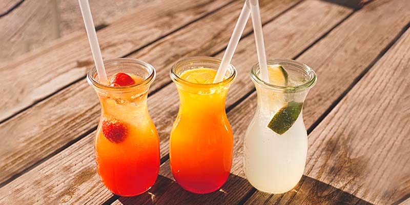 3 copos transparentes de suco de diferente sabores com canudos e frutas