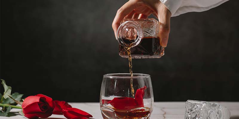 Mão servindo bebida alcolica em um copo com uma petala de rosa