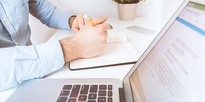 notebook aberto e homem realizando anotações no caderno